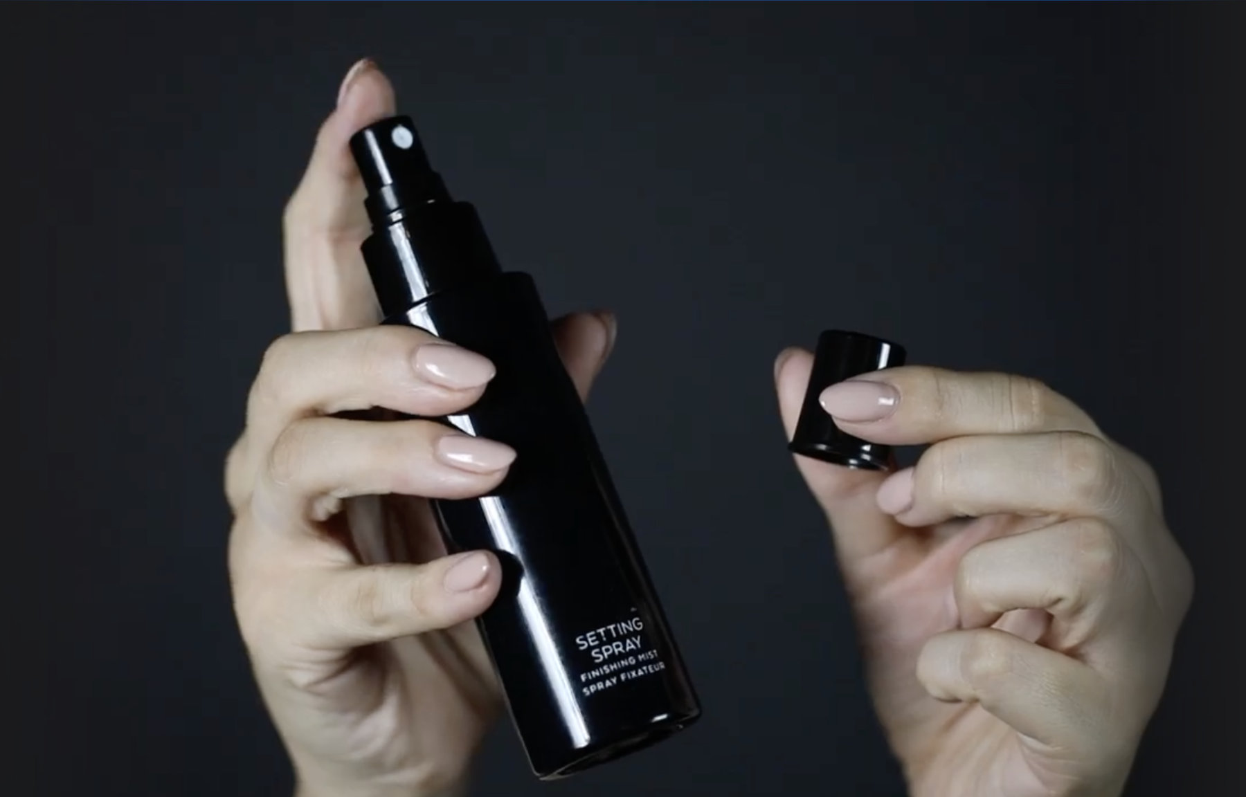 hands holding a black bottle of setting spray